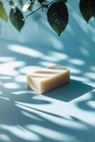 Natural handmade soap placed elegantly on a blue surface with delicate shadow patterns from green leaves photo