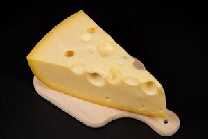 Yellow cheese wedge on wooden cutting board against dark background photo