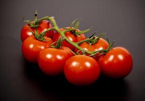 Fresh red tomatoes on a vine arranged on a dark surface photo