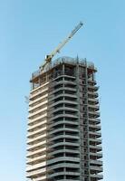 Modern architecture under construction in the city. Unfinished high-rise building with crane and photo
