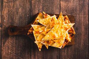 Close up of crispy lavash chips with cheese and garlic on a board on the table top view photo