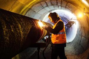 Worker in protective mask welding pipe in tunnel photo