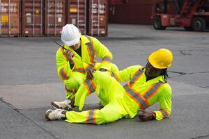 Accident at work concepts, Foreman workers taking care about their colleague lying on the floor at shipping yard photo
