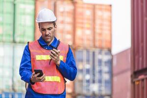 Foreman in hardhat and in safety gear talks on two-way radio control loading containers box from cargo photo