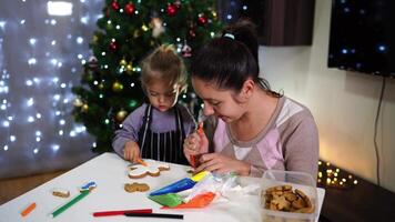 Little girl draws on cookies with a felt-tip pen while her mother applies icing video