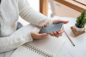 Top view of the hands holding smartphone, sitting at the round marble table with notebook and pencil photo