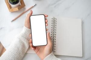 A close up of the pair of hand holding blank screen smartphone over an open notebook on the table. photo