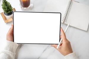 The left hand holding blank screen tablet horizontally with stylus pencil in right hand on the table photo