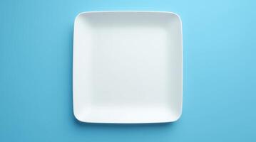 Empty white square plate on blue background. Minimalist tableware, dining, kitchen, food presentation, and restaurant concept photo