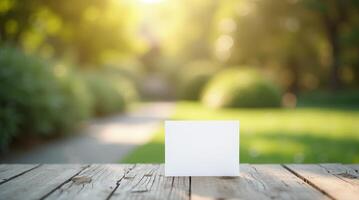 Blank white card on rustic wooden table with blurred green park background. Outdoor invitation or greeting card mockup with copy space photo
