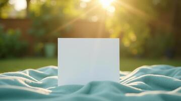 Blank white card on soft fabric with blurred green garden background. Outdoor invitation or greeting card mockup with copy space photo