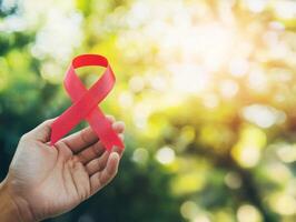 Hand holding a red ribbon in a natural setting during daytime photo