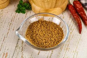 A bowl of mustard seeds and a wooden spoon on a wooden table photo