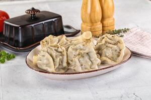 A plate of dumplings on a counter with a knife and a bowl of herbs photo