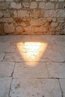 Sunlight creates a triangle pattern on a stone floor next to a stone wall photo
