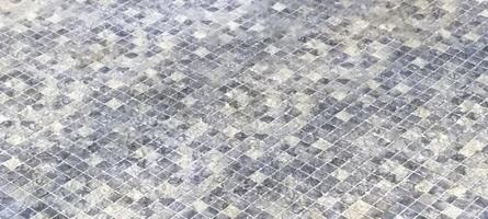 A detailed view of a mosaic-tiled floor covered in water droplets, creating a textured and reflective surface. The small square tiles display various shades of gray, adding depth to the design. photo