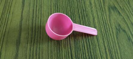 Small Pink Plastic Measuring Scoop on a Green Wooden Surface photo