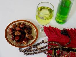 Arrangement featuring a bowl of dates, yellow liquid in a glass, and prayer beads next to a fabric, symbolizing cultural traditions and religious observance in a serene and meaningful setting. photo
