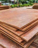 Stacked Sheets of Plywood with Weathered Texture in Outdoor Setting Surrounded by Lush Greenery and Blurred Background photo