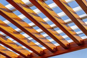 Bright Light and Shadow Play on a Wooden Pergola Structure Against a Clear Blue Sky photo