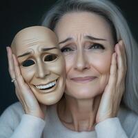 A woman gently holds a mask depicting a happy face while showing a somber expression. Her surroundings are dim, emphasizing her emotional conflict and vulnerability photo