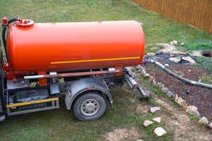 orange tank of sewage disposal machine in courtyard of the house sucks sewage waste from the septic tank well. Waste disposal service, sewage disposal photo