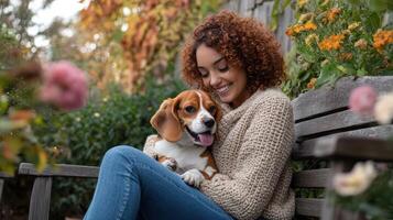 Smiling young woman with curly hair hugging beagle dog on wooden bench in garden photo
