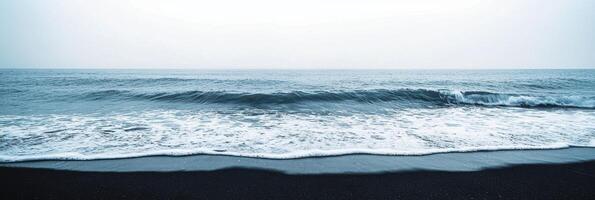 Serene view of ocean waves hitting the black sand beach on overcast day photo