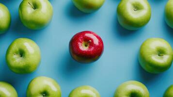 Red apple standing out among green apples on blue background symbolizing unique choice photo