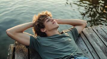 Young blond man relaxing on wooden pier by water during sunny day photo