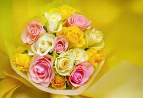 Bouquet of multicolored roses yellow and pink wrapped in yellow paper, bright vibrant roses for sale in yellow background, advertising photo