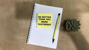 Concept of Be Better Than You Were Yesterday write on sticky notes isolated on Wooden Table. photo