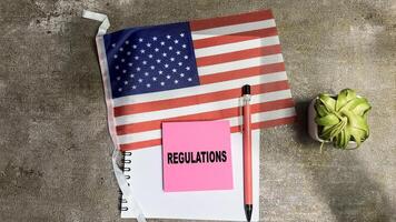 Concept of Regulations write on sticky notes and Flag of the United States isolated on Wooden Table. photo