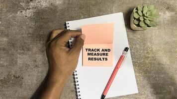 Concept of Track and Measure Results write on sticky notes isolated on Wooden Table. photo
