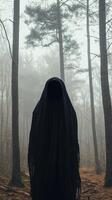 Mysterious hooded figure stands in a foggy forest, tall trees, face hidden. Eerie atmosphere photo