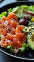 Fresh sashimi and avocado salad with greens and sesame seeds. A mix of ingredients on a black plate photo