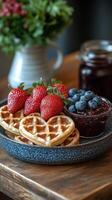 Heart-shaped waffles with strawberries, blueberries, and berry jam on a wooden table, breakfast photo
