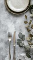 Table setting with plates, cutlery, and eucalyptus leaves, grey table, dining and home decor photo