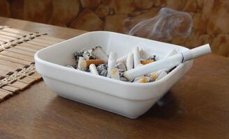 Filter cigarette smokes in white ashtray with butts and ashes closeup angle view photo