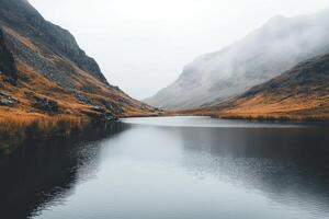 serene lake surrounded by misty mountains, soft grey tones, and crisp reflections create tranquil atmosphere photo
