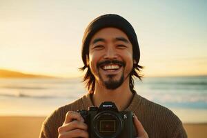 A man smiles while holding a camera on the beach photo