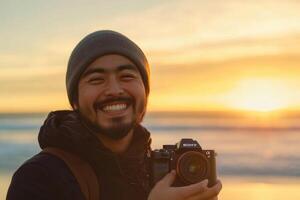 A man smiles while holding a camera at the beach photo