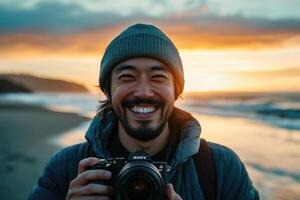 A man smiles while holding a camera at the beach photo