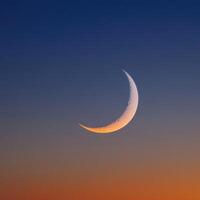 The crescent moon is seen in the sky at sunset photo