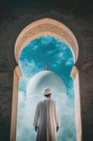 A muslim man in white robe standing in front of a mosque photo