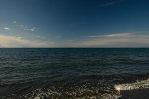 Calm waters stretch endlessly under a serene sky at the beach during golden hour in late afternoon photo
