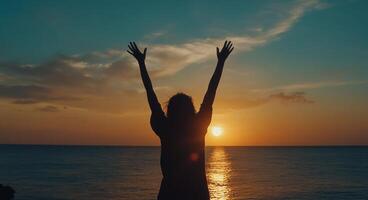 Silhouette of woman with arms raised at sunset photo