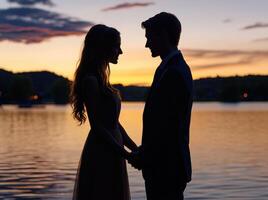 A couple standing in front of a lake at sunset photo
