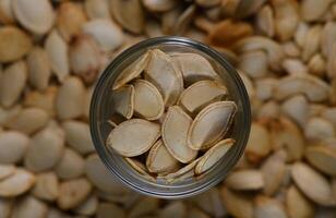 Pumpkin seeds in a glass jar surrounded by a pile of seeds in cozy autumn setting photo