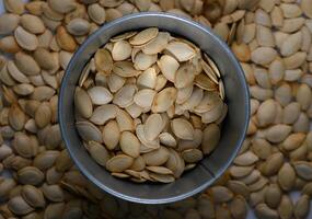 Fresh pumpkin seeds collected in a metal container surrounded by scattered seeds on a wooden surface photo
